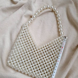 May include: A white pearl beaded handbag with a long pearl strap. The bag is approximately 19 inches wide.