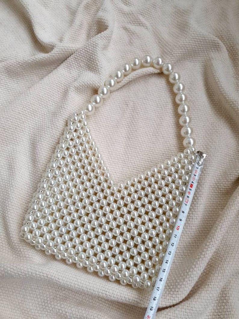 May include: A white pearl beaded handbag with a long pearl strap. The bag is approximately 19 inches wide.