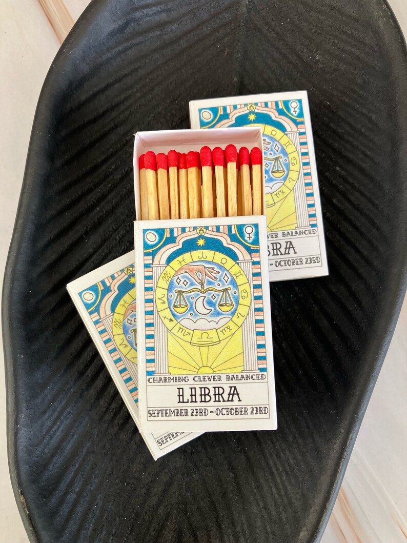 May include: A box of matches with a blue and yellow design featuring the astrological sign Libra. The text on the box reads "Charming Clever Balanced Libra September 23rd - October 23rd".