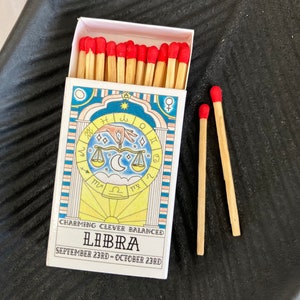May include: A box of matches with a red and white design featuring the astrological sign Libra. The box reads "Charming Clever Balanced Libra September 23rd - October 23rd".