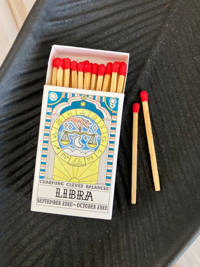May include: A box of matches with a red and white design featuring the astrological sign Libra. The box reads "Charming Clever Balanced Libra September 23rd - October 23rd".