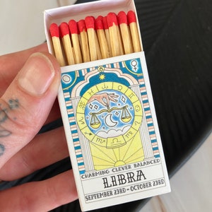 May include: A box of matches with red tips, featuring a colorful illustration of the Libra zodiac sign with the text "CHARMING CLEVER BALANCED LIBRA SEPTEMBER 23RD - OCTOBER 23RD".