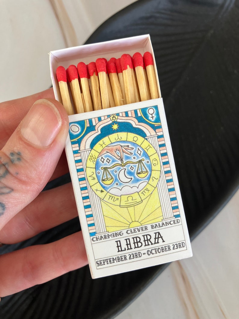 May include: A box of matches with red tips, featuring a colorful illustration of the Libra zodiac sign with the text "CHARMING CLEVER BALANCED LIBRA SEPTEMBER 23RD - OCTOBER 23RD".