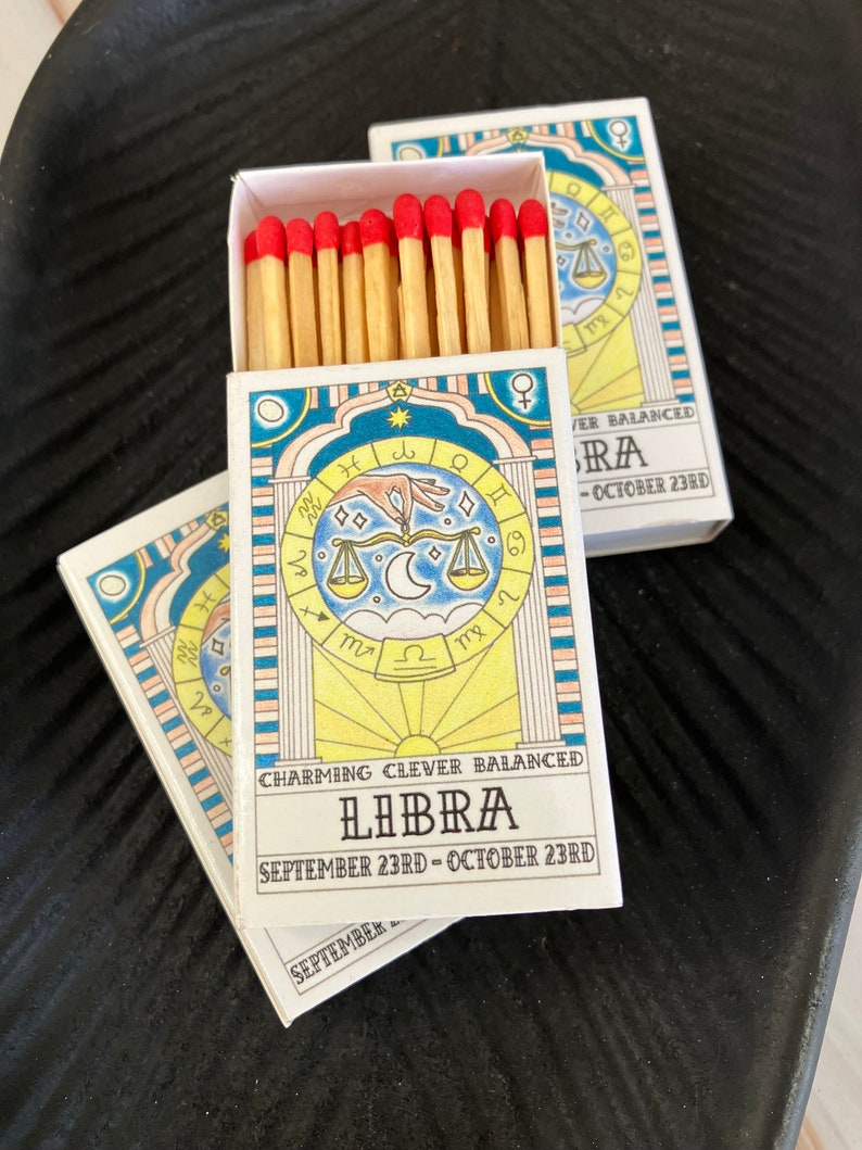 May include: A box of matches with a blue, yellow, and white design featuring the astrological sign Libra. The box has the text "Charming Clever Balanced Libra September 23rd - October 23rd".