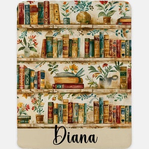 Può includere: Una morbida coperta con un design ad acquerello di librerie piene di libri d'epoca e piante in vaso. La coperta ha un bordo color crema con il nome "Diana" in corsivo. La tavolozza dei colori comprende marroni, verdi e rossi.