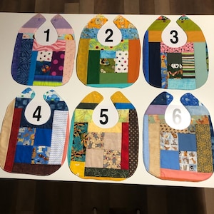 May include: Six handmade baby bibs with patchwork designs. Each bib features a unique combination of colorful fabric squares and patterns, including floral, animal, and geometric prints. The bibs are numbered 1 through 6 on white circles.