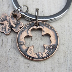 Könnte beinhalten: Ein Schlüsselanhänger aus Kupfer mit einem ausgeschnittenen vierblättrigen Kleeblatt. Der Penny ist mit 1963 datiert und trägt die Inschriften "In God We Trust" und "Liberty". Der Schlüsselanhänger hat auch einen kleinen vierblättrigen Kleeblatt-Anhänger aus Kupfer.