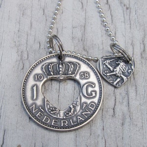 May include: Silver necklace with a heart-shaped pendant featuring a Dutch coin with the inscription "1958 NEDERLAND" and a smaller pendant with a lion and shield.