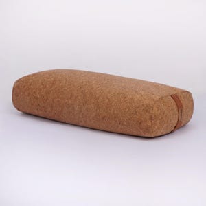 Puede incluir: Un cojín de yoga rectangular hecho de corcho. El cojín es de color marrón claro con bordes redondeados y una correa de cuero marrón en un extremo. Diseñado para yoga y meditación, mide aproximadamente 60 cm de largo.