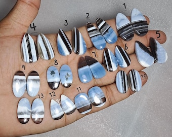 May include: A collection of polished opal gemstones in various shapes and patterns. The opals feature a mix of blue, white, brown, and black colors. The gemstones are displayed on a hand, showcasing their unique designs and textures.