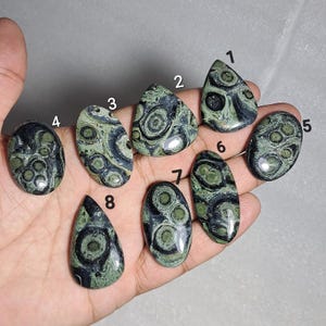 以下が含まれることがあります： ユニークな模様の研磨された宝石が8つ表示されています。 宝石の形は様々で、しずく型、楕円形、三角形などがあります。 主な色は緑と黒で、円形や渦巻き模様があります。 これらの宝石は、ジュエリー作りやコレクションに最適です。
