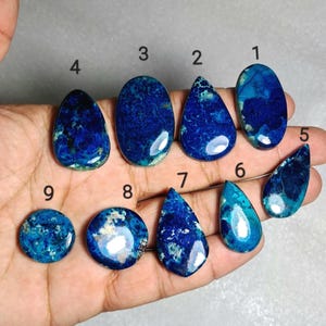 Puede incluir: Nueve piedras preciosas pulidas de varias formas, incluyendo ovaladas, en forma de lágrima y redondas. Las piedras muestran un color azul profundo con vetas azules y blancas más claras. Las piedras preciosas se muestran sobre un fondo neutro.