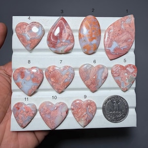 May include: A selection of polished gemstones in diverse shapes, including hearts and an oval. The stones feature pink, white, and orange colours, with distinctive veining. A US quarter is included for size comparison.