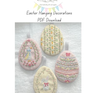 Può includere: Quattro decorazioni pasquali a forma di uovo ricamate. Ogni uovo presenta un design unico, tra cui un'anatra, carote, un coniglietto e motivi floreali a strati. Le uova sono in colori pastello con un nastro a quadretti per appenderle. Il testo recita "Easter Hanging Decorations PDF Download."