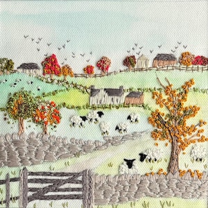 May include: A textile embroidery depicting a rural landscape with rolling green hills, stone walls, and a wooden gate. The scene features several white and black sheep grazing in fields, scattered trees with orange and red foliage, and small houses.