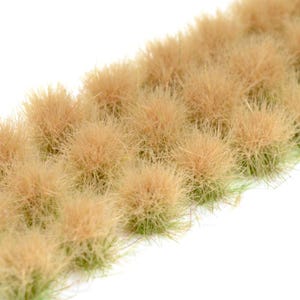 Może przedstawiać: Zbliżenie na kilka kępek suszonej trawy w kolorze brązowym. Trawa ma włóknistą teksturę i jest ułożona w małe, zaokrąglone skupiska. Białe tło podkreśla naturalne odcienie trawy. Idealna do modelarstwa lub miniaturowego krajobrazu.
