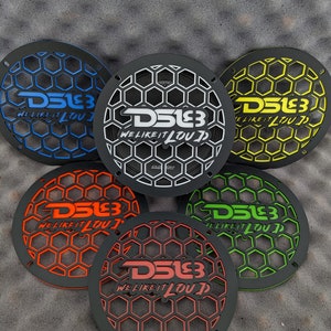 Könnte beinhalten: Fünf schwarze Lautsprechergitter mit Wabenmustern und dem Text "DS18 WE LIKE IT LOUD" in Blau, Gelb, Orange, Grün und Rot. Die Gitter sind kreisförmig.