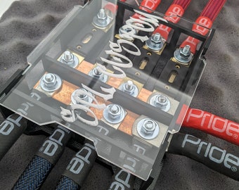 May include: A black and clear electrical component with multiple bolts and wires. The wires are red and blue, with the text "Pride" visible on the red wires. The component has the text "Audio" in white.