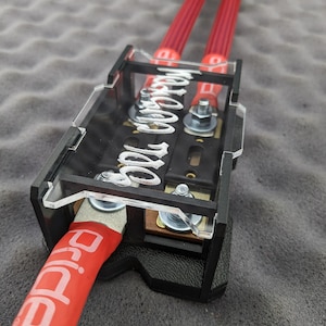 以下が含まれることがあります： 赤色のケーブルが付いた黒と透明の電気部品。ケーブルの端は黄色と青です。コンポーネントには「Pride」の文字が白で印刷されています。コンポーネントは灰色の表面にあります。