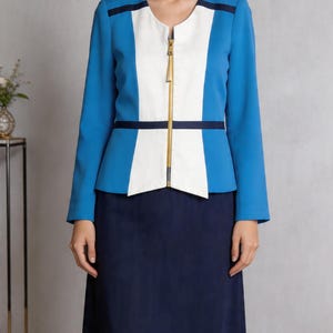 May include: A smart blue, white, and navy suit. The jacket features a gold zip and a colour-block design. The skirt is navy blue. This is a business or formal wear outfit.
