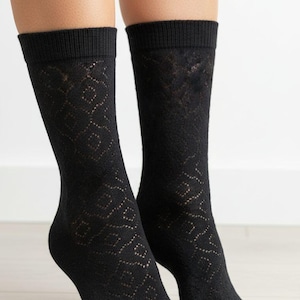 May include: A pair of black crew socks with a diamond pattern. The socks are made of a sheer material and have a ribbed cuff. The socks are worn on a person's feet.