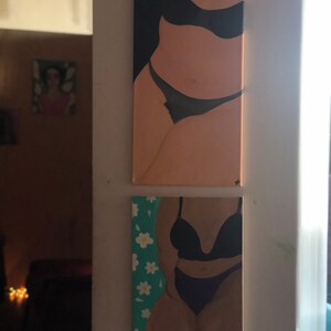May include: Two paintings of figures in lingerie. The top painting is a vertical canvas with a nude figure in black lingerie. The bottom painting is a smaller canvas with a figure in black lingerie and a teal background with white flowers.