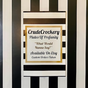 May include: A rectangular sign featuring a black and white horizontal striped pattern with a central gold-bordered white square. The text reads: CrudeCrockery, Plates Of Profanity, &ldquo;What Would Nanna Say?&rdquo;, Available On Etsy, Custom Orders Taken.