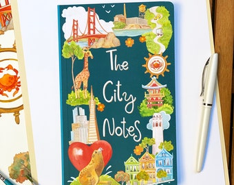 May include: A teal blue notebook with a watercolor illustration of the Golden Gate Bridge, a giraffe, a sea lion, and other San Francisco landmarks. The text "The City Notes" is written in white on the cover. The website "www.OlgaAkbarova.Art" is printed at the bottom of the notebook.