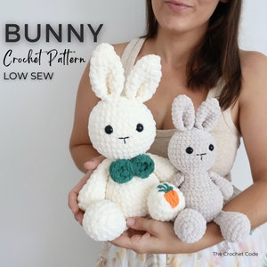 Op de afbeelding: Twee gehaakte konijnenknuffels, een witte met een groene strik en een grijze, vastgehouden door een persoon. Het witte konijn houdt een kleine oranje wortel vast. De afbeelding bevat de tekst "BUNNY Crochet Pattern LOW SEW" en "The Crochet Code".