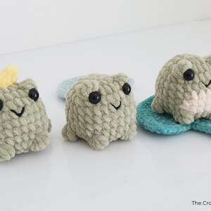 May include: Three handmade crochet frog plushies in shades of green. One frog has a yellow crown, another sits on a blue lily pad, and all have black eyes and smiling faces. The Crochet Code is in the bottom right.