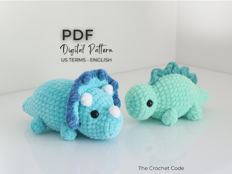 May include: Two crocheted dinosaur toys. One is a light blue triceratops with a dark blue frill and white horns. The other is a light green dinosaur with a spiky back. The text "PDF Digital Pattern US TERMS - ENGLISH" is at the top.
