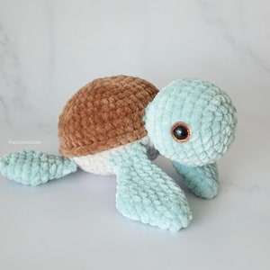 K&ouml;nnte beinhalten: Ein geh&auml;keltes Pl&uuml;sch-Schildkr&ouml;tenspielzeug mit brauner Schale, wei&szlig;em Unterleib und hellblauen Gliedma&szlig;en. Die Schildkr&ouml;te hat schwarze Augen mit braunen Pupillen.