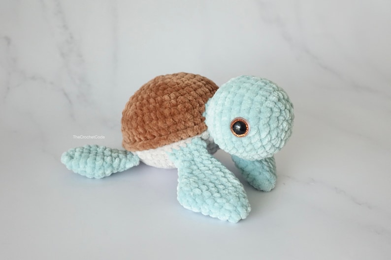 K&ouml;nnte beinhalten: Ein geh&auml;keltes Pl&uuml;sch-Schildkr&ouml;tenspielzeug mit brauner Schale, wei&szlig;em Unterleib und hellblauen Gliedma&szlig;en. Die Schildkr&ouml;te hat schwarze Augen mit braunen Pupillen.