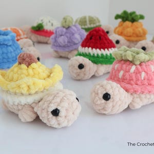 May include: A collection of crocheted turtle toys, each with a different fruit-themed shell. The turtles are in various colors, including pink, yellow, blue, and green. The toys have black button eyes and are displayed on a white surface.