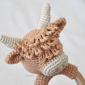 May include: A crocheted cow rattle toy in brown and white. The toy has a wooden ring attached to the bottom.