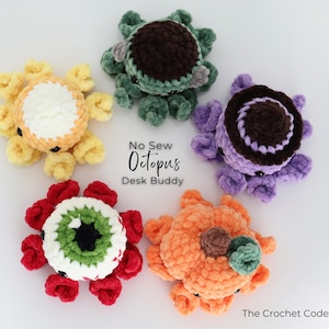 Puede incluir: Cinco pulpos de ganchillo dispuestos en c&iacute;rculo. Las figuras son de color amarillo, verde oscuro, morado, rojo y blanco, y naranja. El texto en el centro dice No Sew Octopus Desk Buddy, y el texto en la esquina dice The Crochet Code.