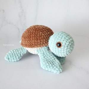 K&ouml;nnte beinhalten: Eine geh&auml;kelte Pl&uuml;schschildkr&ouml;te mit braunem Panzer und hellblauem K&ouml;rper. Die Schildkr&ouml;te hat ein einzelnes braunes Auge.