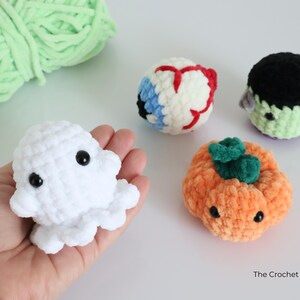 May include: A selection of handmade crochet Halloween-themed plush toys. Includes a white ghost, an eyeball, a Frankenstein's monster, and an orange pumpkin with a green stem. The Crochet Code is visible in the bottom right corner.