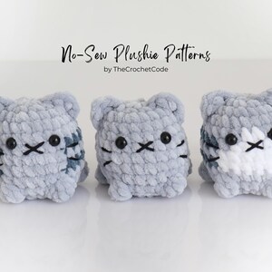 May include: Three handmade, gray plush cat toys with black embroidered facial features and striped details. The toys are displayed on a white surface. The text "No-Sew Plushie Patterns" is above the toys.