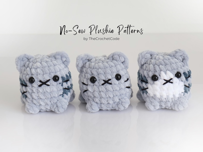 May include: Three handmade, gray plush cat toys with black embroidered facial features and striped details. The toys are displayed on a white surface. The text "No-Sew Plushie Patterns" is above the toys.