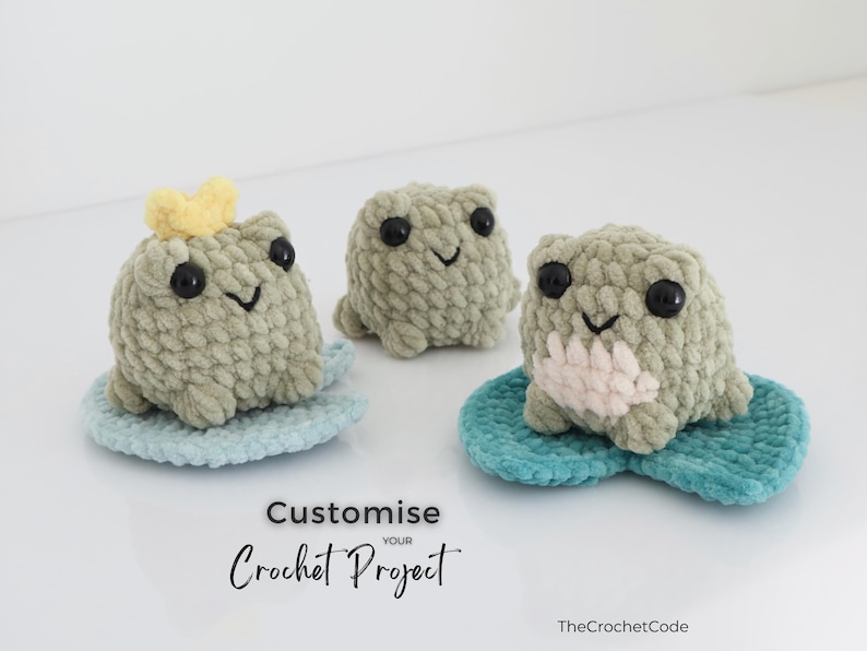 May include: Three handmade crochet frog plushies in shades of green, each with black eyes and a smiling face. One frog wears a yellow crown. They sit on blue lily pads. The text "Customize your Crochet Project" is visible.