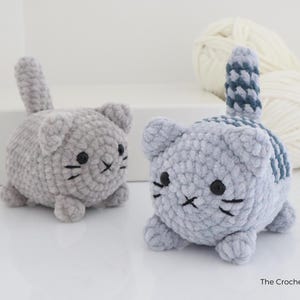 May include: Two handmade crochet cat toys. One is solid gray, the other has a blue and gray striped tail and back. Both have black eyes and whiskers. The toys are small and round, and appear to be made of soft yarn.