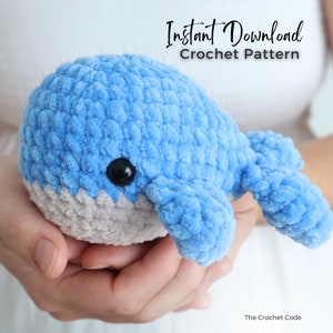 Op de afbeelding: Een handgemaakte, lichtblauwe gehaakte walvis met een grijze buik en zwarte knoopogen. De zachte, pluche walvis wordt in open handen gehouden. De afbeelding bevat de tekst "Instant Download Crochet Pattern".