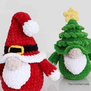 Puede incluir: Dos gnomos navide&ntilde;os de peluche. Uno es rojo con barba y ribete de sombrero blancos, cintur&oacute;n negro y hebilla dorada. El otro es un gnomo de &aacute;rbol de Navidad verde con una estrella amarilla y barba blanca. The Crochet Code.