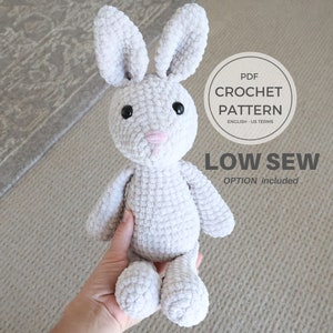 May include: A crocheted gray bunny rabbit with black eyes and a pink nose. The bunny is sitting on a hand. The image includes the text "PDF CROCHET PATTERN ENGLISH - US TERMS LOW SEW OPTION included".