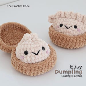 May include: Two crocheted plush dumplings in brown baskets with light pink tops, black embroidered eyes, and small pink cheeks. The text The Crochet Code and Easy Dumpling Crochet Pattern is visible on the white background surrounding the items.