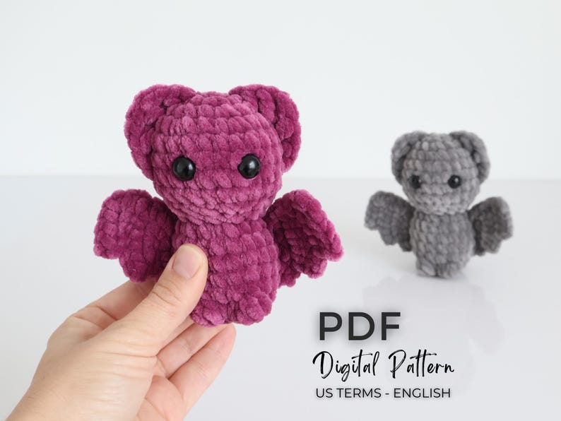 K&ouml;nnte beinhalten: Zwei geh&auml;kelte Fledermaus-Pl&uuml;schtiere, eine in tiefem Lila und die andere in Grau, mit schwarzen Sicherheitsaugen und ausgebreiteten Fl&uuml;geln. Der Text "PDF Digital Pattern US TERMS - ENGLISH" wird angezeigt.
