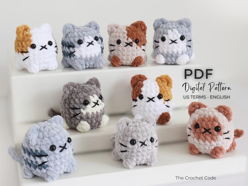 May include: A collection of handmade crochet cat plushies in various colors, including white, gray, and brown. Each cat has a unique pattern and embroidered facial features. The image also includes the text "PDF Digital Pattern US TERMS - ENGLISH".