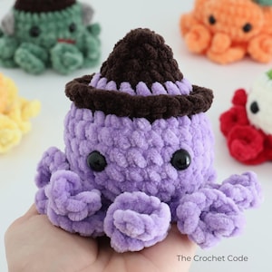 Puede incluir: Un peluche de pulpo tejido a ganchillo de color morado con un sombrero marr&oacute;n oscuro, ojos de pl&aacute;stico negro y tent&aacute;culos rizados. El peluche es parte de una colecci&oacute;n de criaturas tejidas, con el texto The Crochet Code visible abajo.