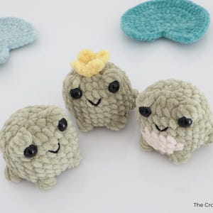 May include: Three handmade crochet creatures with black eyes and smiling faces. One has a yellow flower on its head, and another has a pink patch. Two blue and teal crochet shapes are also in the image. The Crochet Code is in the bottom right corner.
